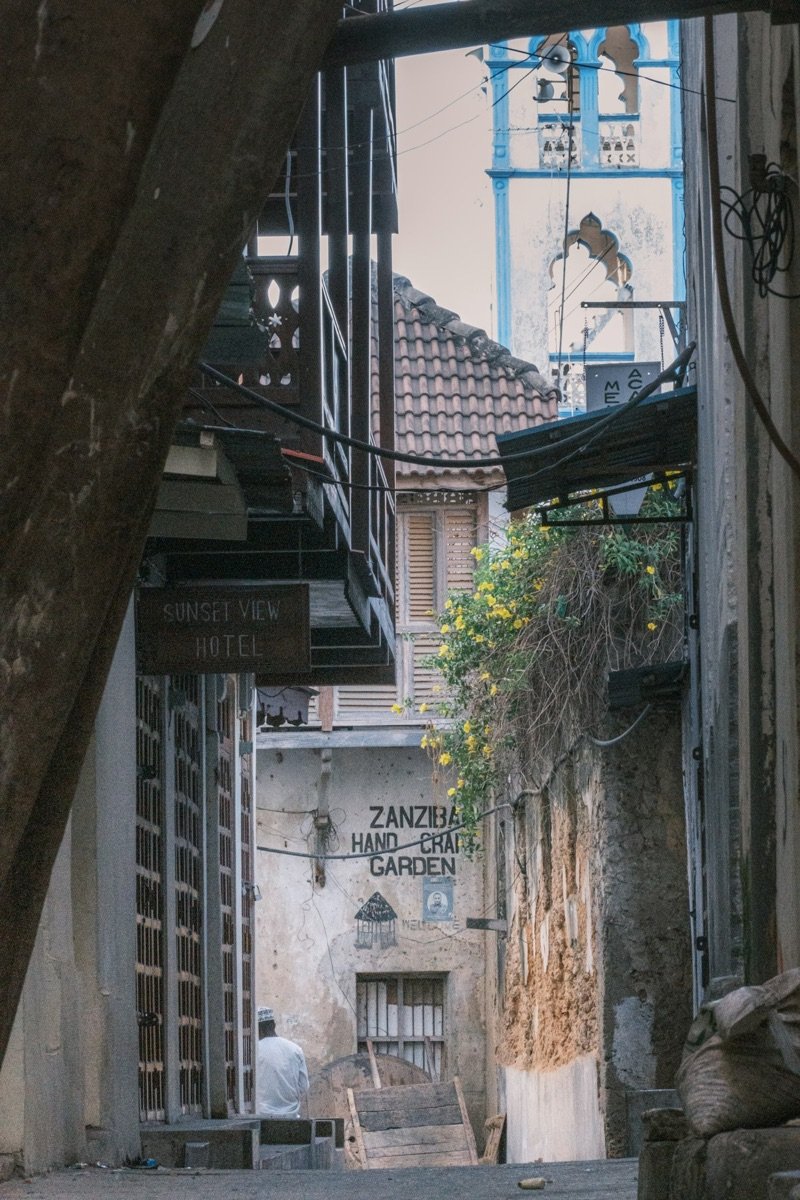 Narrow alley with carved wooden doors and Zanzibar Hand Craft Garden sign in Stone Town