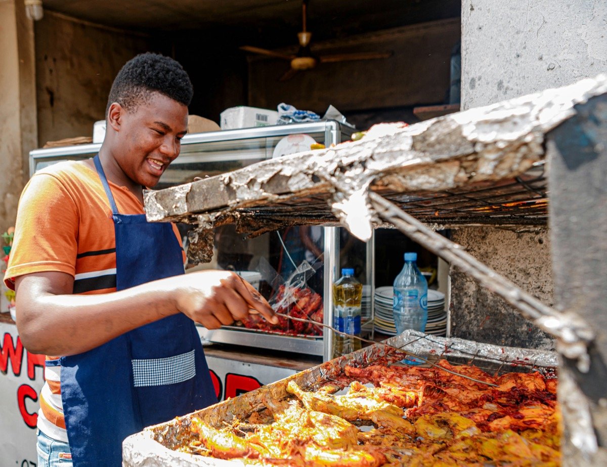 Man cooking grilled meat over a charcoal grill at a street food stall in Dar es Salaam