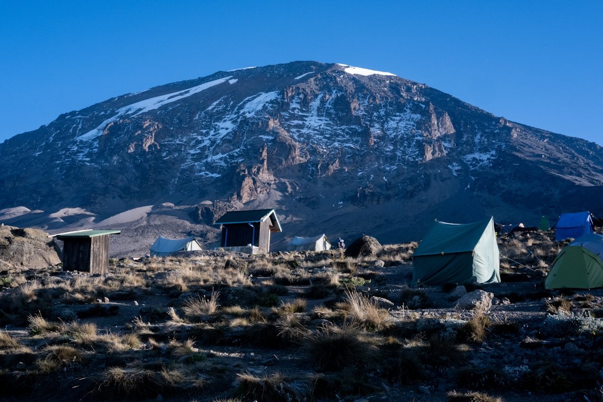 Tents set up in a high-altitude Kilimanjaro camp with the snow-covered summit visible against a clear blue sky, Tanzania