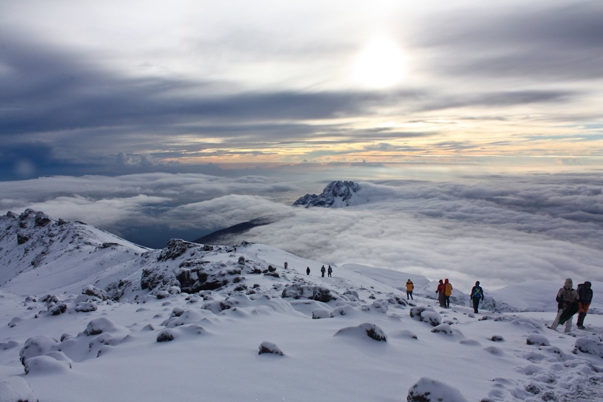 Trekkers descending across a vast snow-covered plateau on Kilimanjaro at dusk with cloud sea below, Tanzania