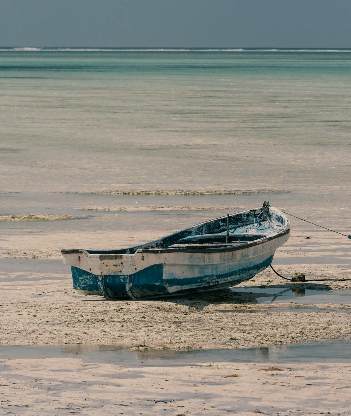 Blue and white painted wooden dhow boat resting on a white sand Zanzibar beach shore