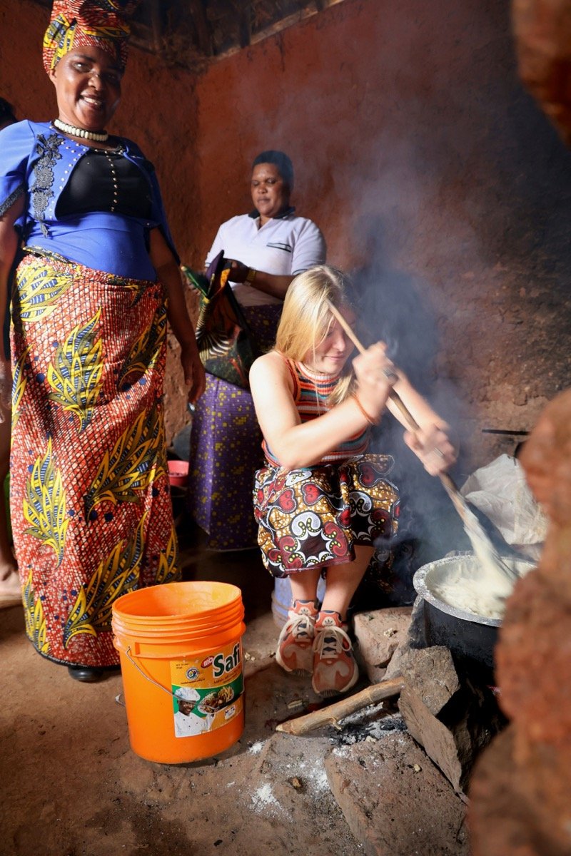Tanzanian women cooking ugali over an open fire in a traditional kitchen