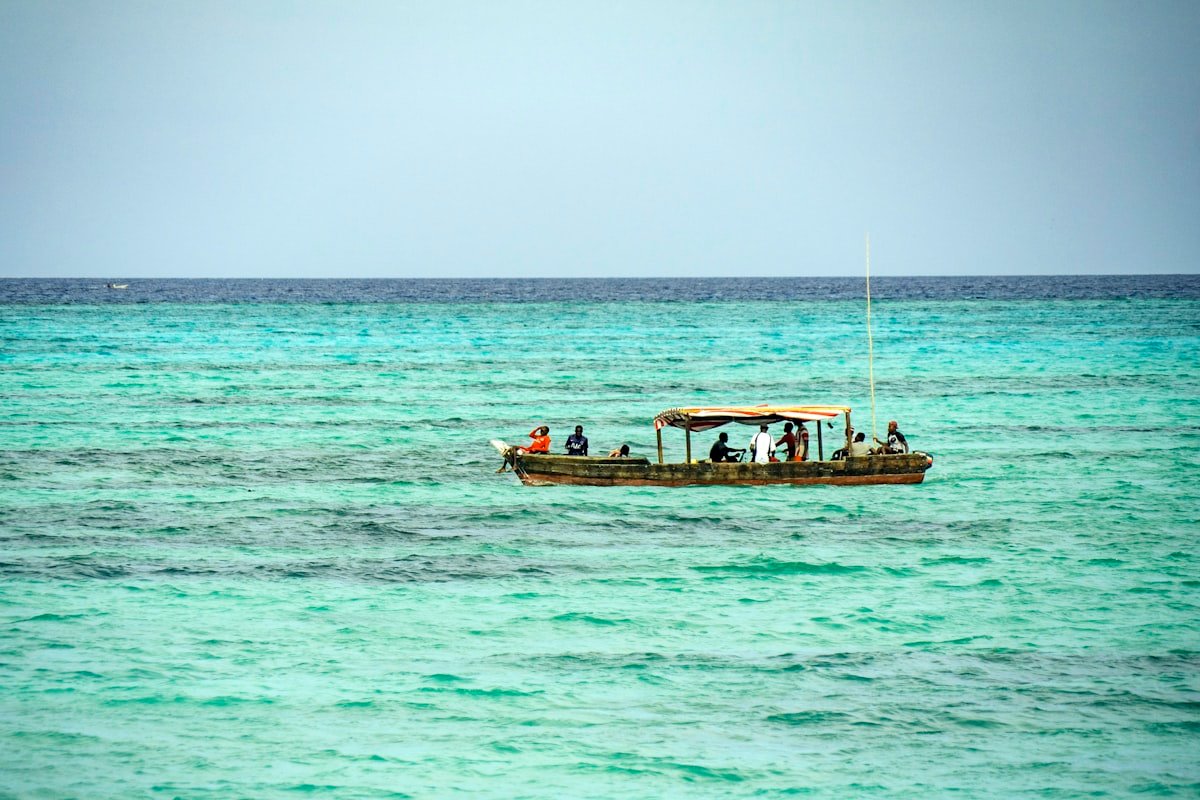 Group of tourists on a traditional wooden dhow boat on turquoise Indian Ocean water, Zanzibar, Tanzania