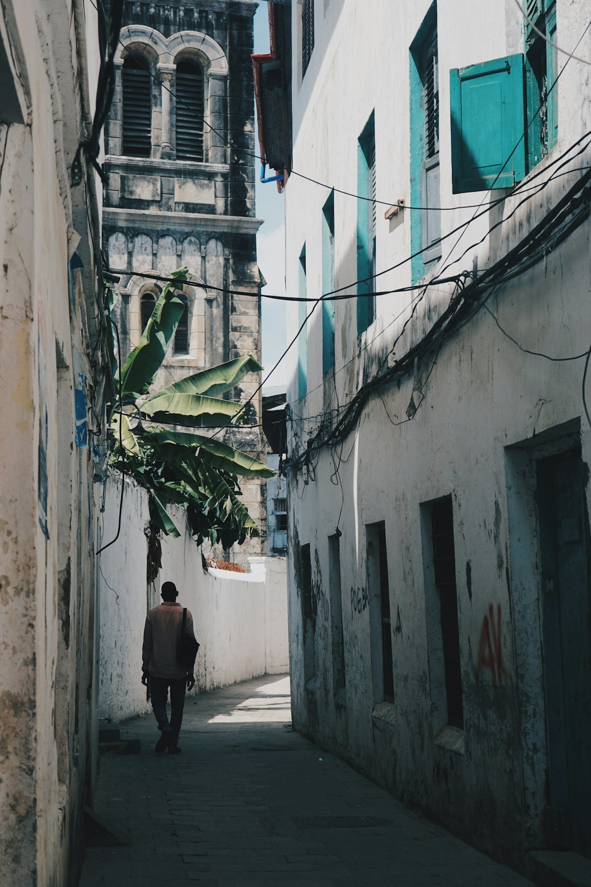 Man walking down a narrow alley with carved wooden buildings and a bell tower, Stone Town, Zanzibar